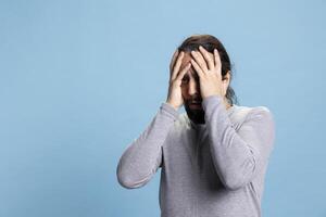 Horrified young guy in shock getting really scared and worried about something, being distraught and fearful against blue background. Afraid terrified man being frightened, horror reaction. photo
