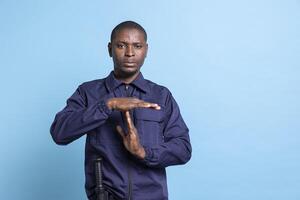 African american guard asking for a break with a timeout symbol in studio, feeling overworked with burnout on duty. Man in agent uniform presenting a pause gesture for relaxation. photo