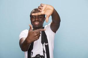 African American man standing and making a frame hand gesture towards camera. Smiling male photographer forms a rectangle with his fingers, looking through it before capturing a shot with his DSLR. photo