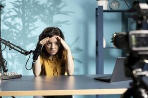 Content creator feeling upset, sharing concerning story during live broadcast, talking to audience. Woman getting headache from stress, talking with viewers, ranting and arguing with subscribers photo