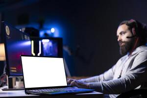 Mockup laptop device next to man playing high FPS videogame with spaceship shooting laser streams at asteroid. Isolated screen notebook near gamer using crosshair overlay to hit targets in SF game photo