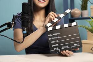 Closeup of woman in vlogging studio presenting a clapperboard to the camera, using a microphone for her product review. The scene captures the essence of digital content creation and media production. photo