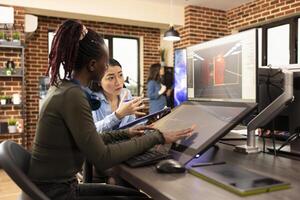 Diverse digital artists working on graphic design and multimedia projects, using a computer and touchscreen monitor. Black and asian women developing creative applications in collaborative workspace. photo