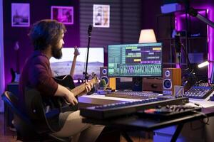 Music composer playing guitar to create songs and mix them after, having fun with musical instrument and controls in his home studio. Skilled producer songwriter creating a track, creative sounds. photo