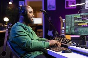 Confident music producer operating on mixing console in home studio, producing new tunes for a song and editing volume levels in daw platform. Sound engineer recording audio files. photo