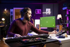 Sound producer learning new piano notes on midi controller, playing acoustic melody on electronic keyboard synthesizer with greenscreen on display. Singer watches tutorials to play music. photo