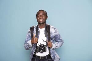 Cheerful black photographer enthusiastically gestures a thumbs up, ready for his next project. African american cameraman smiles brightly, equipped with a backpack and DSLR camera. photo