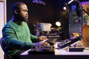 Skilled music producer creating new songs on midi controller synthesizer, working with mixing console and professional software on pc. Male artist using piano and mastering acoustical tunes. photo