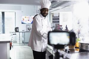 negro cocinero grabación en línea Cocinando demostración para un vlog tutorial, exhibiendo comida preparación y gastronomía tecnicas Ayudar remoto estudiantes Maestro multa comida culinario habilidades. foto