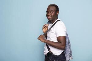 Confident african american man poses in a studio, adjusting his suspenders with effortless style. His charismatic smile and expressive stance create a striking portrait against a isolated backdrop. photo
