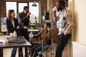 Colleagues enjoying casual office chatter, bonding over shared experiences in modern startup environment. Laughter fills the modern workspace as multiethnic employees take a break at the office desk. photo