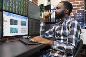 Young forex trader analyzing real time financial data on different computer screens at night in office. Male entrepreneur in deep thoughts, focused on the trading software and stock market charts. photo