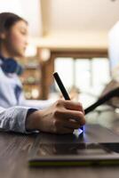 Closeup of asian designer using stylus on digital drawing pad to fine tune and edit photos. Selective focus on individual adjusting color balance with graphic tablet, enhancing images for magazine use photo