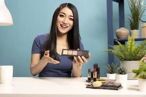 Smiling beauty influencer with eyeshadow palette, recording a cosmetics tutorial, presenting makeup products with a professional setup. Ideal for social media, branding, and digital content marketing. photo