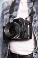 Extreme closeup of a black camera. Selective focus on DSLR hanging from the neck of an individual in a denim jacket, with selective focus on the lens, highlighting intricate details. photo