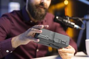 Close up shot of V mount battery held by tech expert filming technology review. Focus on charging device having its specifications analyzed by reviewer in blurry background photo