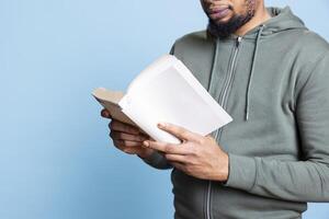 African american reader enjoying leisure time with a literature book, feeling happy reading about fantasy characters. Confident young man relaxing with literature, analyzing synopsis. Close up. photo