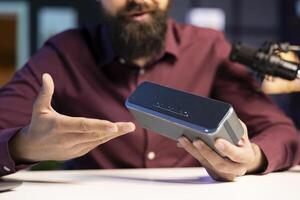 Man doing technology review of wireless portable speaker for internet vlogging channel. Close up shot of music playing device held by influencer showing it to his subscribers photo