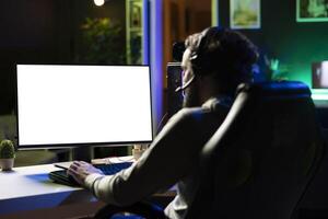 Man having fun by using isolated screen computer monitor to play singleplayer videogame. Professional gamer using mockup PC desktop to complete levels in game, talking with friends though headphones photo