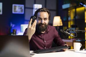 Cheerful tech expert filming review for online channel in apartment studio, analyzing office mouse for audience. Happy content creator recommending computer peripheral device photo