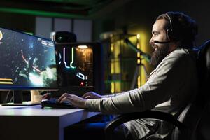 Upbeat man having fun with his friends playing videogames, chatting online using headphones microphone. Jolly gamer using computer with powerful graphics to enjoy multiplayer experience with teammates photo