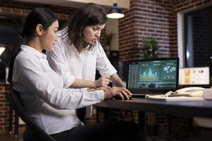 A professional discussion between coworkers, collaborating on a business project, using research data on laptop. White woman stands and reviews details as her colleagues scrolls through the document. photo