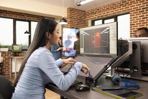 Asian game developer creates professional content in the production department, using touchscreen display. Skilled woman focuses on developing 3D game scenes and environments, utilizing multi screens. photo