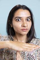Indian young adult asking for a break with the timeout symbol in studio, showing her control and determination. Tired serious person indicating pause gesture against blue background. photo