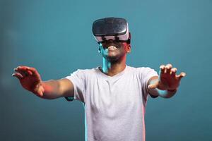 Happy male model enjoying an interactive game with a VR headset, reaching out toward the camera. Excited black man experiencing cutting edge 3D technology for virtual entertainment. photo