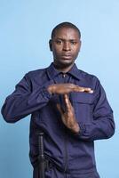 African american security guard doing a timeout symbol to take a break from his duty, experiencing burnout and working in tension. Serious unhappy male agent asking for a pause in studio. photo
