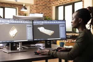 African american technical expert prototyping machinery and constructing engine models digitally. Black female engineer designing mechanical gears using CAD software in brick wall office. photo