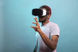 Black man exploring virtual reality, using goggles to interact with futuristic elements. Enthusiastic male gamer wearing VR headset, enjoying immersive technology, fully engaged in a digital world. photo