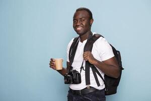 Smiling male model with a backpack and disposable cup looking directly at the camera, exuding confidence and readiness for a new creative project. Black photographer standing with his gear and coffee. photo