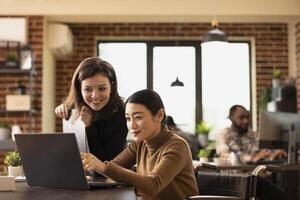 Multiethnic employees working together at office desk, reviewing financial data on laptop. An inclusive workspace where caucasian manager and asian wheelchair user discuss business growth strategies. photo