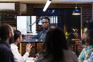 Professional black man seen on digital monitor during call with colleagues. Male entrepreneur collaborates remotely with diverse team, discussing marketing strategy and project deadlines. photo