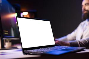Man having fun by using isolated screen laptop to play multiplayer videogame. Close up of gamer using mockup notebook device to complete levels in game, talking with friends though headphones photo