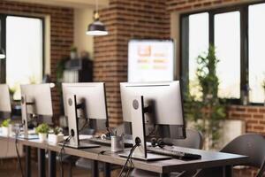 Unoccupied office space showcasing a modern setup with multiple desktop monitors. The neatly organized desks and brick wall background create a professional atmosphere for startup company. photo