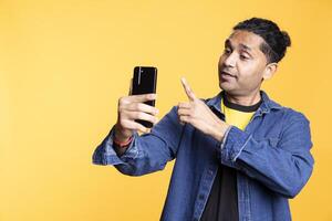 Radiant indian man saluting his friend over call connection, doing friendly gestures and smiling in studio. Happy joyous person acting friendly communicating with people on web conference. photo