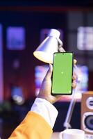 Close up of person in workspace watching videos on social media using green screen mobile phone. Woman scrolling on touchscreen mockup smartphone, using social network website on smartphone photo