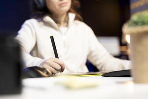 Photo editor using graphic tablet to edit images, delivering visually appealing final product, listening to music. Freelancer wearing headphones browsing through photographs, close up