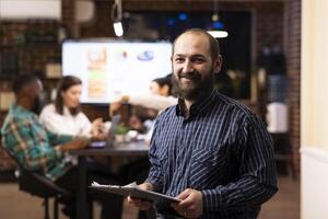 Determined businessman in checkered shirt ready to review project planning details in office. The modern workspace, late night teamwork and digital analytics highlight productivity. photo
