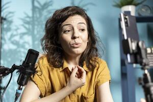 Media star hosting online show in well lit studio, shooting vlog using phone on selfie stick. Woman presenting informations during streaming service broadcast, close up shot photo