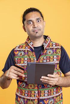 Portrait of furious client dejected after lacking necessary money while trying to buy stuff on internet using tablet. Livid customer frustrated after getting transaction rejected, studio backdrop photo