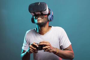 Young man wearing VR headset and wireless headphones, utilizing technology for gaming activity. Male individual virtually playing a game with controller, fully immersed in futuristic simulation. photo