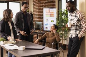 Multiracial professionals in a creative startup office taking a moment to unwind, chatting and laughing together during a break. African american man with glasses, sharing a story to his team. photo
