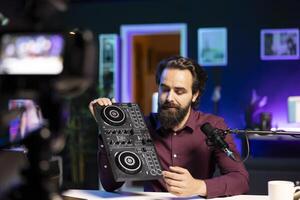 Artist filming DJ mixing tutorial, showing fans examples of sampling on sound controller. Man presenting settings on turntables mixer musical equipment in apartment studio photo