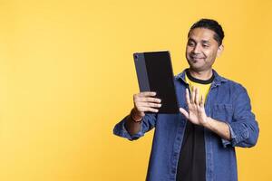 Friendly adult enjoying an entertaining conversation with friends on web call, laughing and feeling happy during call meeting against studio background. Waving hand on camera. photo