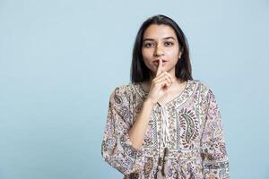 Authoritative woman doing shushing hand gesture in front of camera, demanding secrecy and being irritated by noise. Indian person complaining, placing finger on lips and doing quiet warning sign. photo