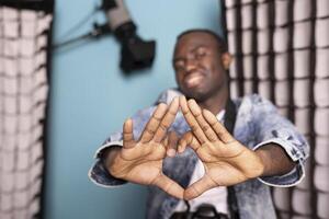 Closeup of african american man hands making a heart sign towards the camera, emphasizing a warm and friendly gesture. Smiling black male photographer forming a love shape with his fingers in studio. photo