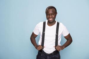 African american man casually dressed, posing in a studio with his suspenders adding a vintage charm. Black male model standing confidently against an isolated background, exuding personality. photo